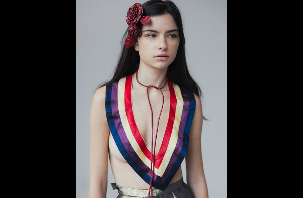 Model wearing a striped, sleeveless top with a deep V-neck and a red flower in her hair.