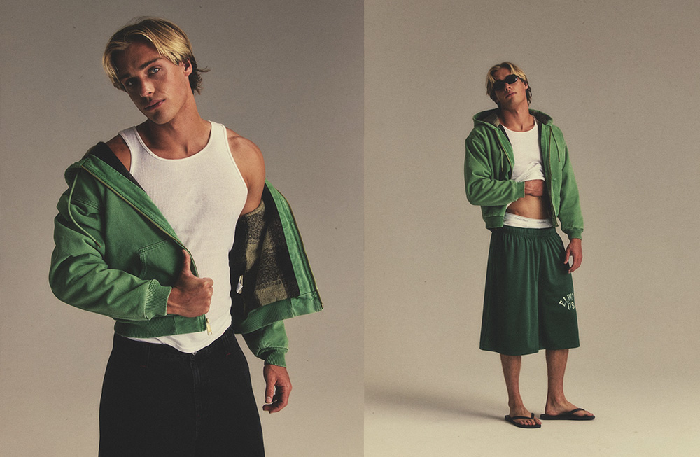 Woman modeling a green jacket with white top and black skirt in studio.